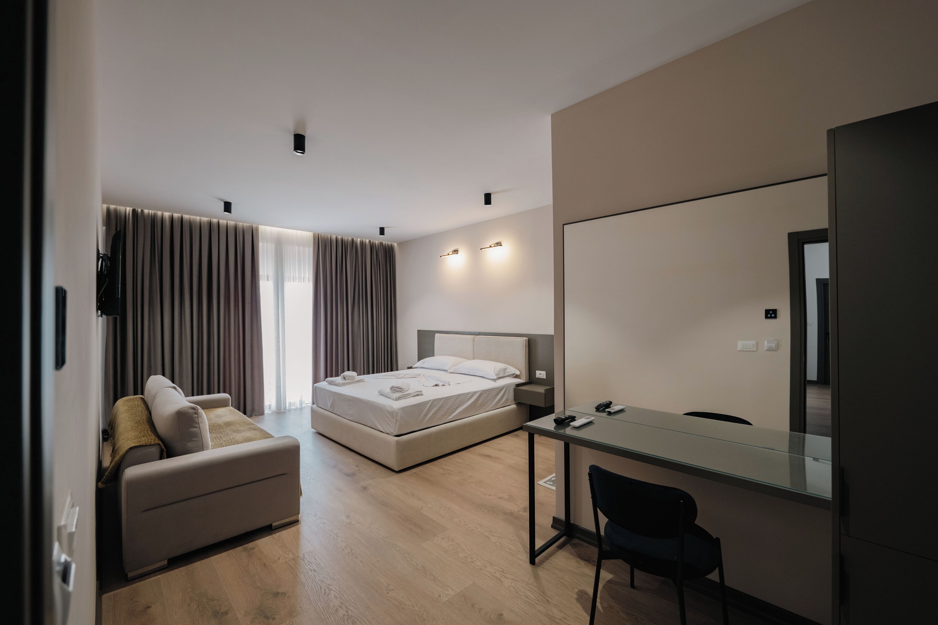 A modern hotel room with a bed, a sofa, a desk, and a large mirror.