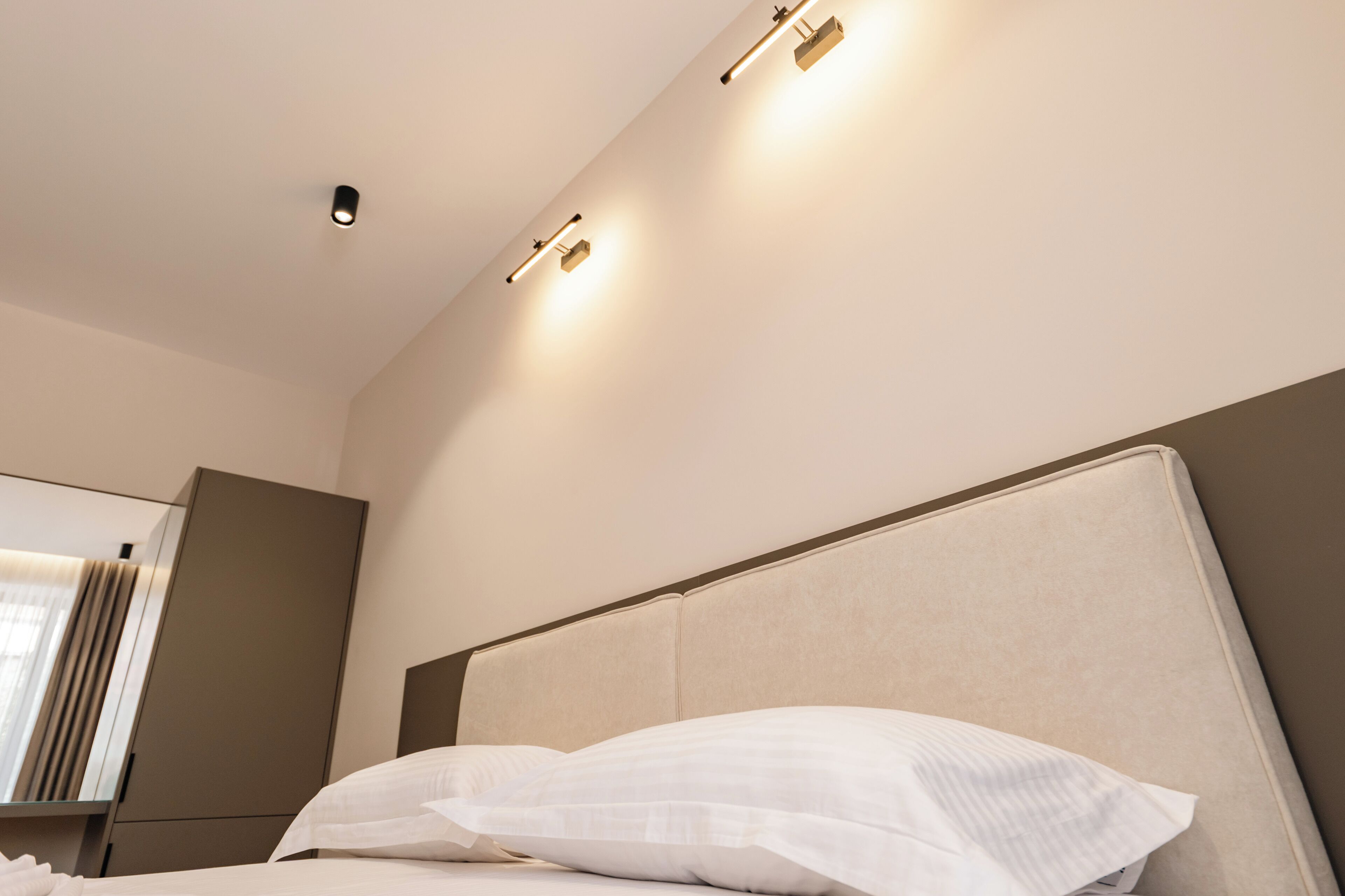 A modern hotel room with a large bed, a headboard, and a wall-mounted light fixture.