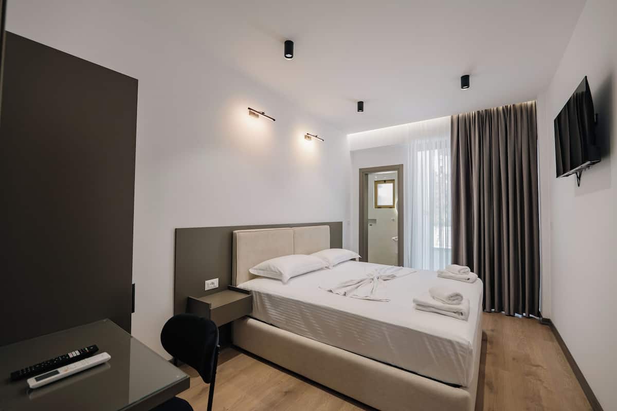 Habitación de hotel moderna con cama, mesita de noche, televisor y escritorio con control remoto.
