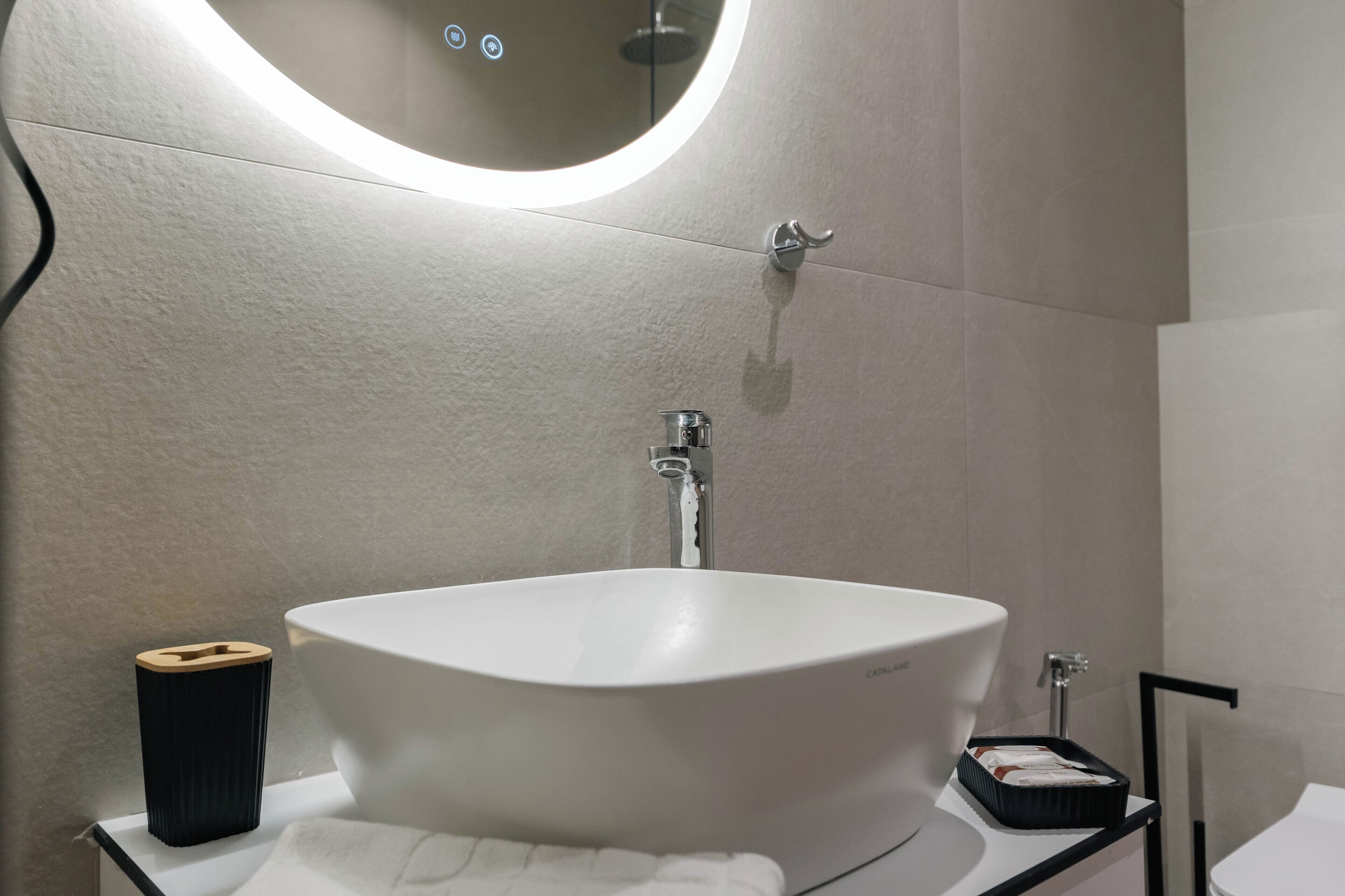 A bathroom with a white sink, a round mirror, and a black soap dish.