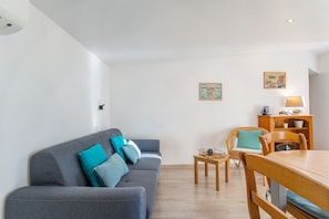 Un salon moderne avec un canapé gris, des coussins turquoise, une table à manger en bois et deux chaises.
