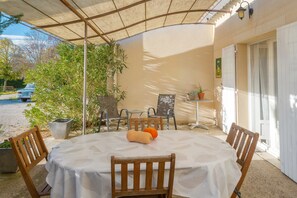 Un espace extérieur abrité, aménagé pour les repas, avec une table, des chaises et des plantes en pot.
