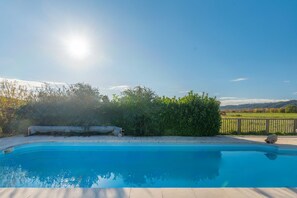 Une piscine d’un bleu éclatant, bordée d’une terrasse en bois, entourée de verdure et offrant une vue sur des collines lointaines.
