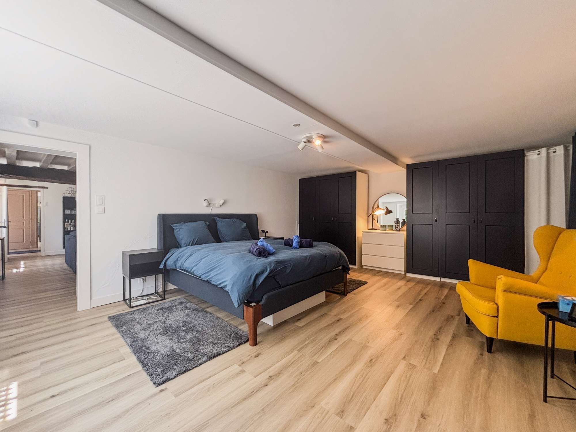 Un dormitorio moderno con una cama, mesitas de noche, un tocador, un espejo y un sillón amarillo.