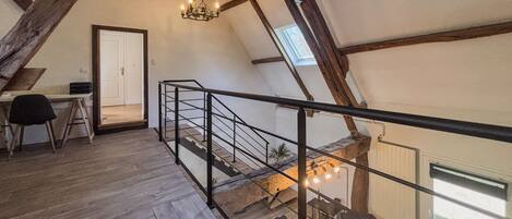 A loft-style room with exposed wooden beams, a staircase, a desk, and a view of the outdoors.
