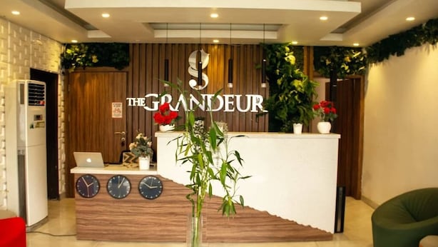 A reception desk with a clock, a laptop, and a vase with flowers. - The Grandeur  (Lagos)