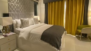 A modern hotel room with a bed, bedside tables, a chair, and a large window with curtains. - The Grandeur  (Lagos)