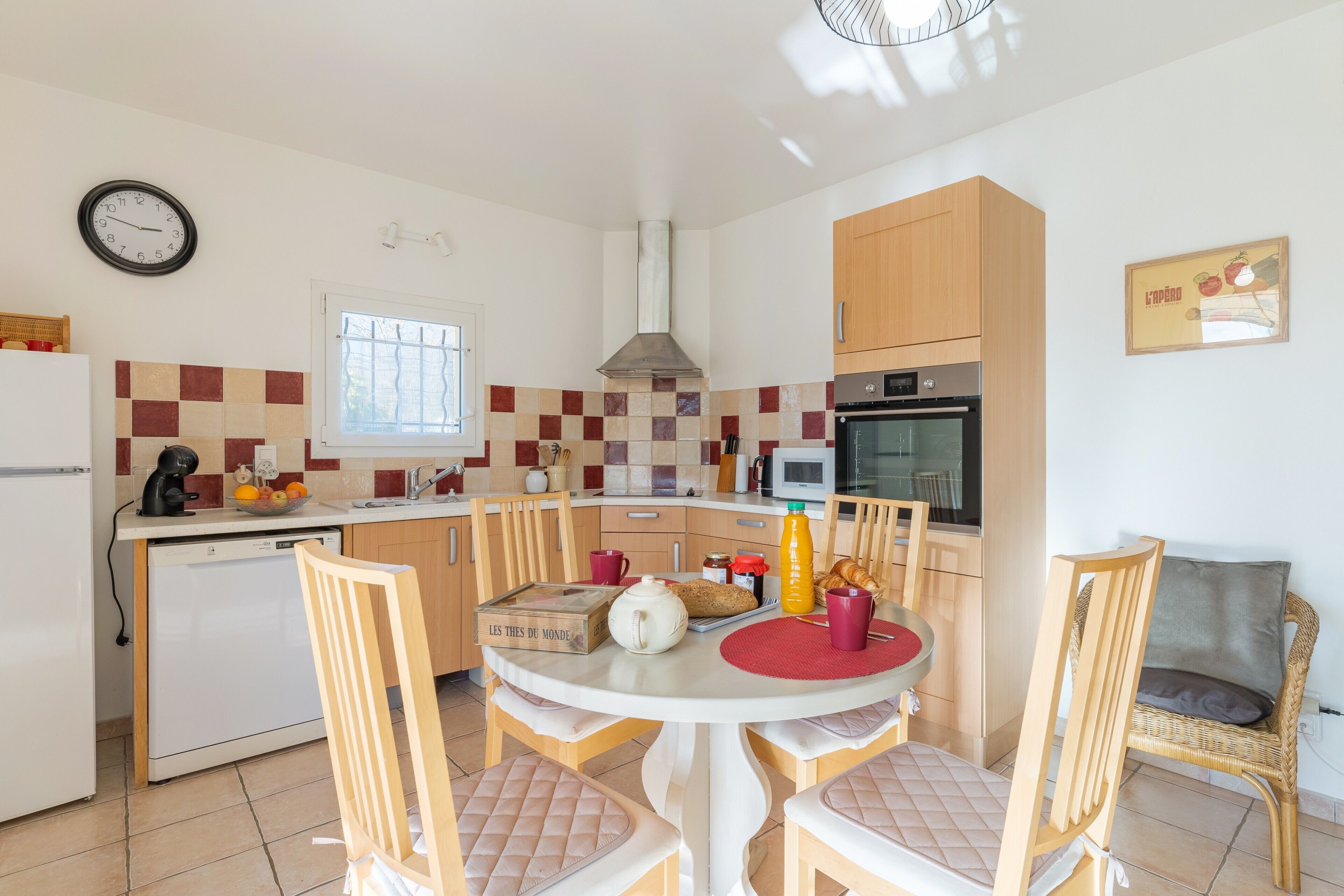 A kitchen with a dining table, chairs, a clock, a microwave, and a stove.