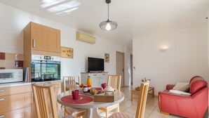 A modern kitchen with a microwave, oven, and dining area with chairs and a table. - Gîte 'Le Petit Étang' with Shared Pool, Private Terrace and Air Conditioning (Gréoux-les-Bains)
