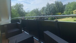 A balcony with wicker furniture, a metal railing, and a view of a green landscape with trees and a clear sky. - Matti vacation home in the Lusatian Lakeland (Schipkau)