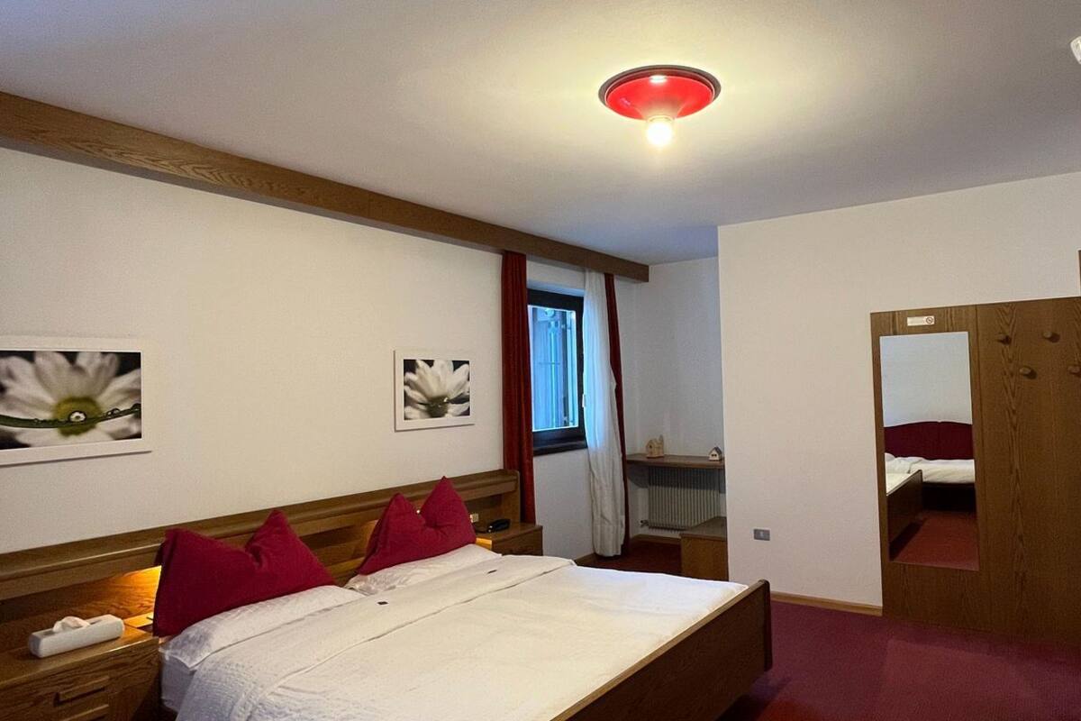 A bedroom with a wooden bed, red pillows, a nightstand, a mirror, and a red ceiling light.