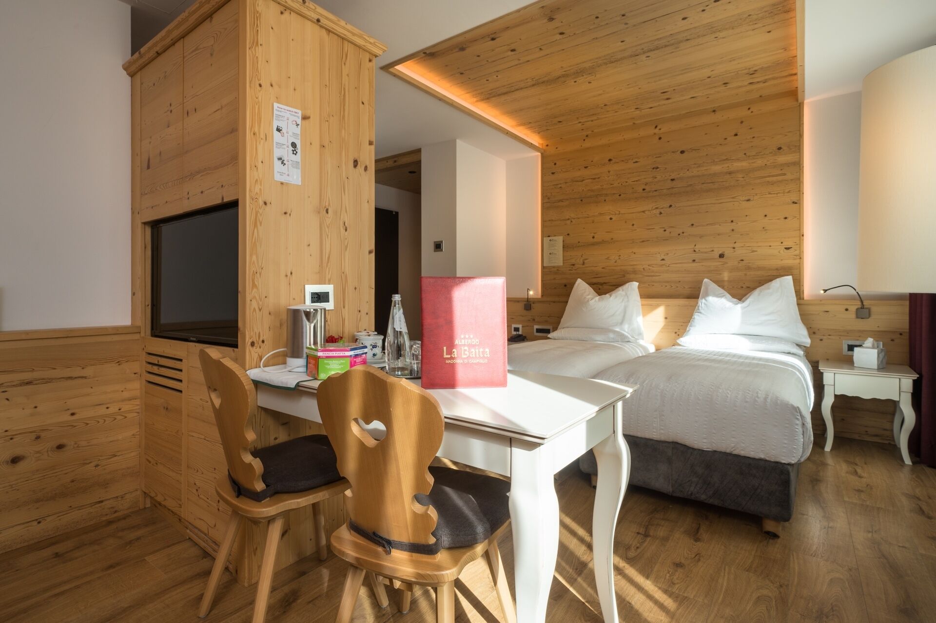 Habitación de hotel con techo de madera, cama con ropa blanca, escritorio con silla y televisor.