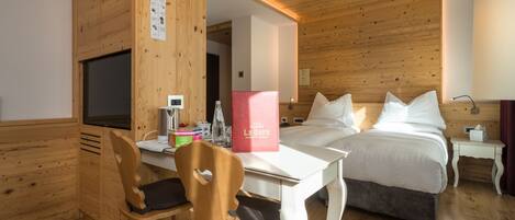 Habitación de hotel con techo de madera, cama con ropa blanca, escritorio con silla y televisor.