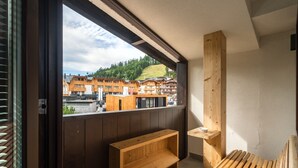 A balcony with a wooden bench and a small table, overlooking a town with traditional buildings and a hill in the background. - Hotel La Baita (Madonna di Campiglio)