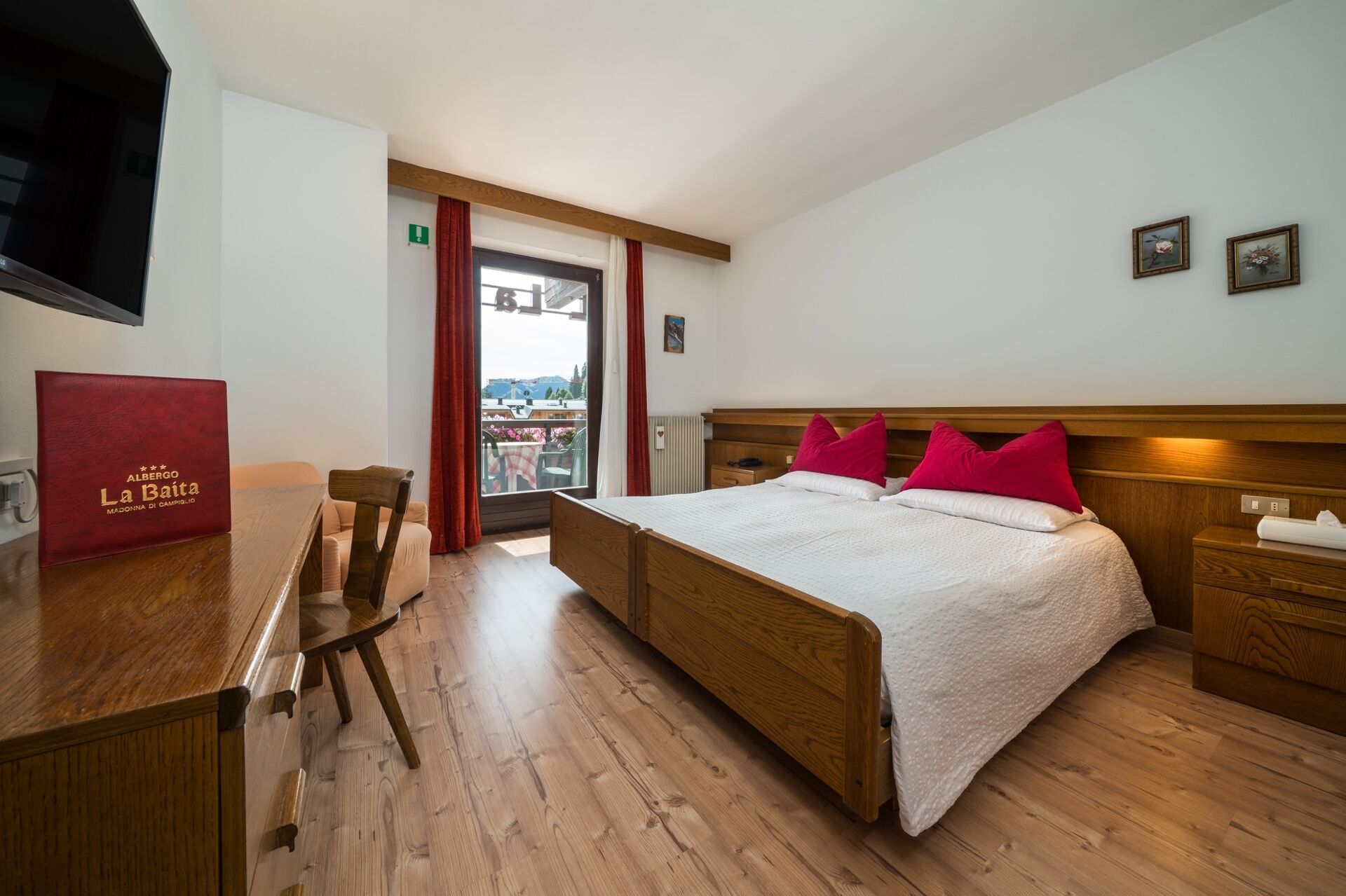 A hotel room with a wooden bed, a desk, and a chair. There is a window with a view of the outside.
