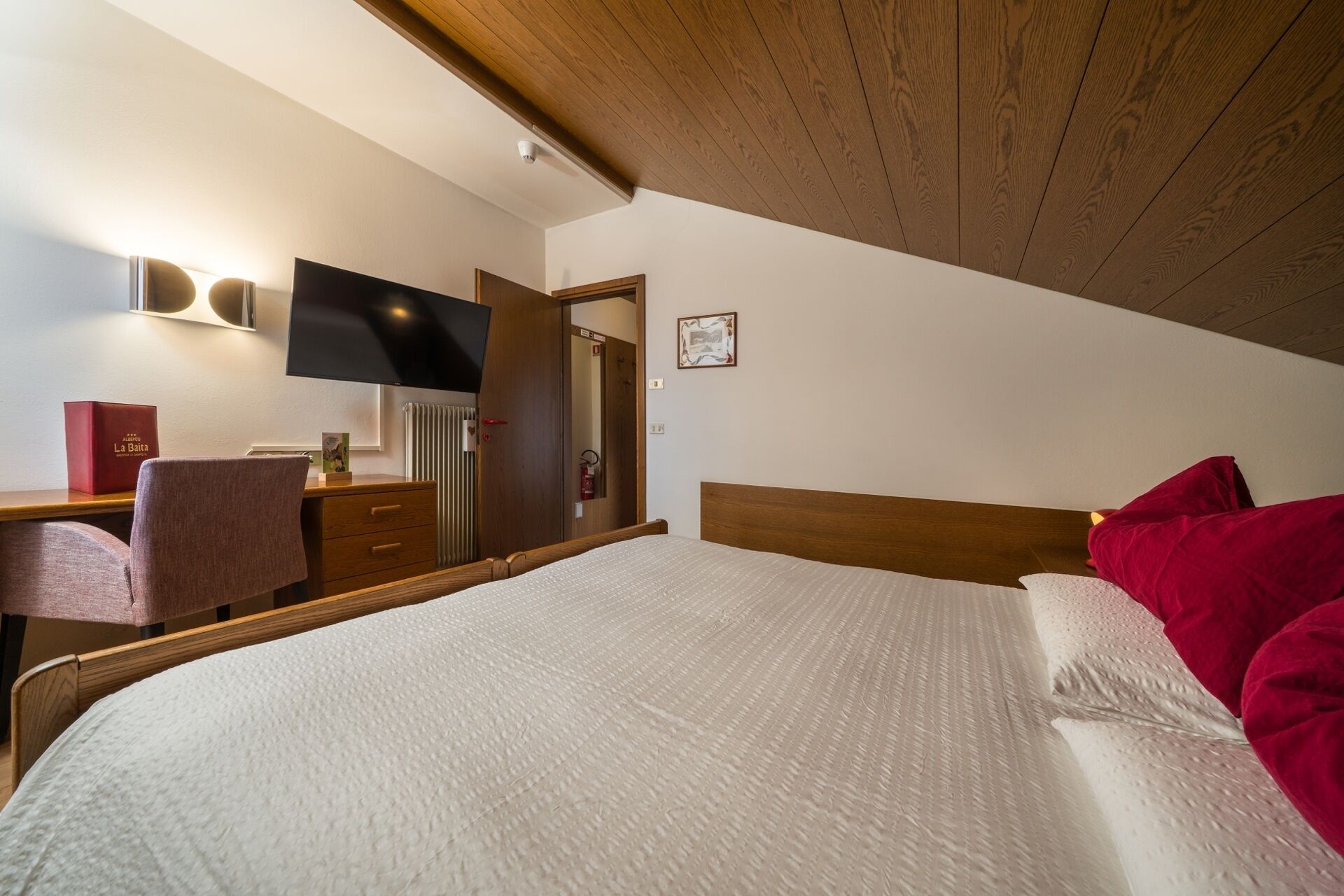 A bedroom with a bed, a desk, a chair, a television, and a framed picture on the wall.
