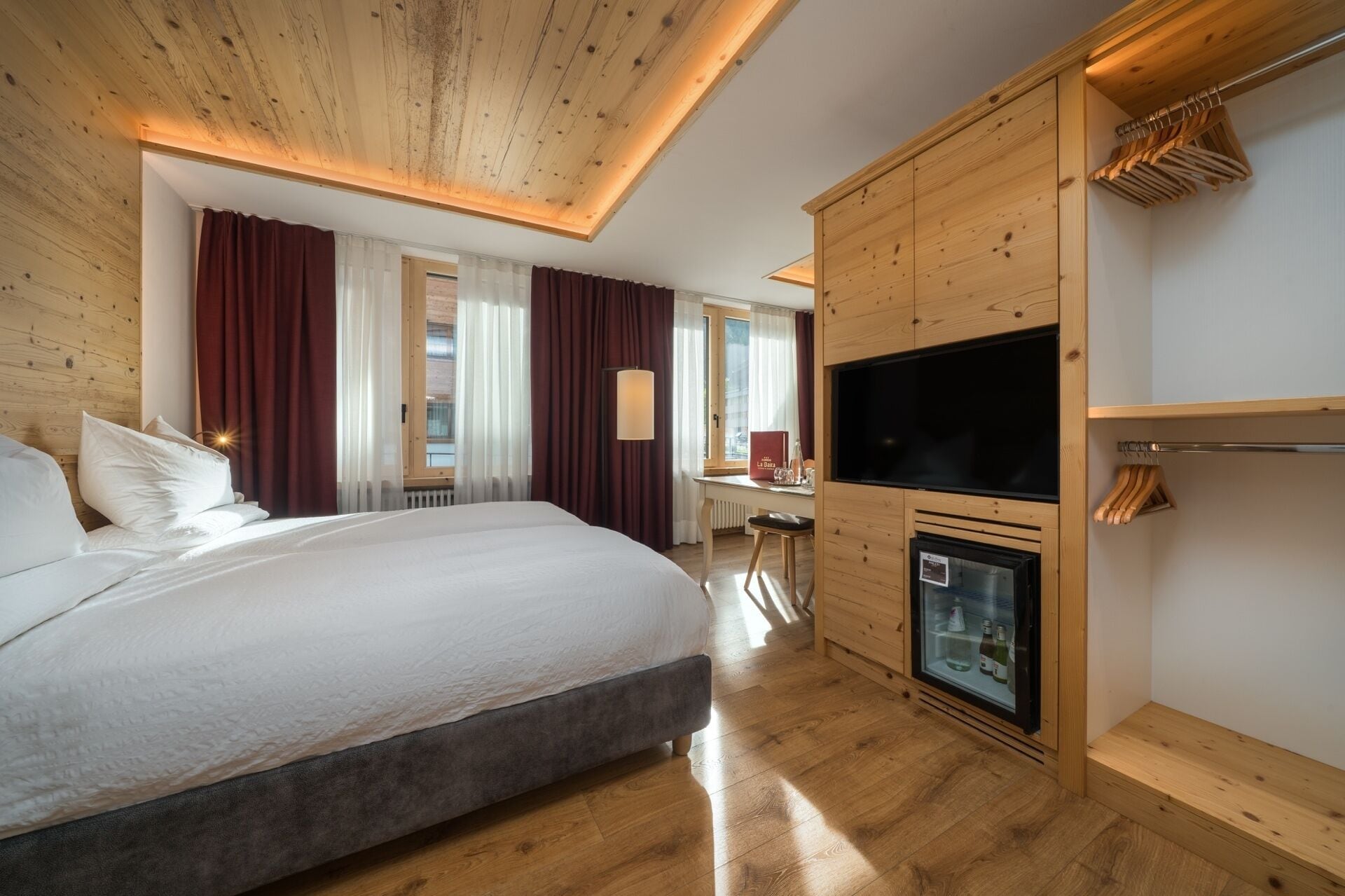 A hotel room with a large bed, wooden ceiling, a TV, and a minibar.
