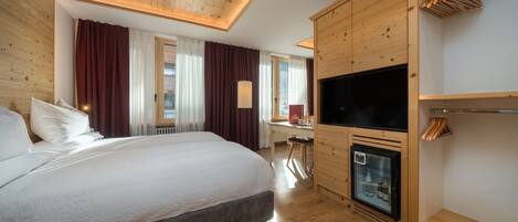A hotel room with a large bed, wooden ceiling, a TV, and a minibar.
