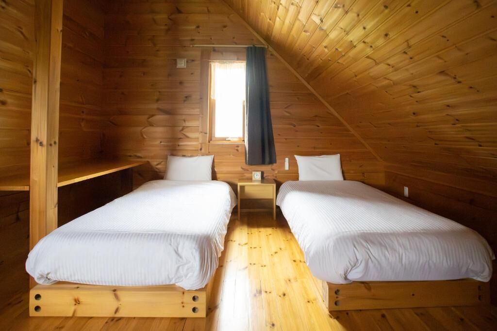 A cabin with two wooden beds, a small window with a curtain, and a wooden floor.