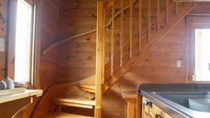 A wooden interior with a spiral staircase, wooden walls, and a kitchen area with cabinets.