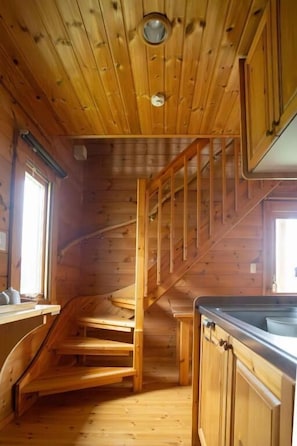 A wooden interior with a spiral staircase, wooden walls, and a kitchen area with cabinets.