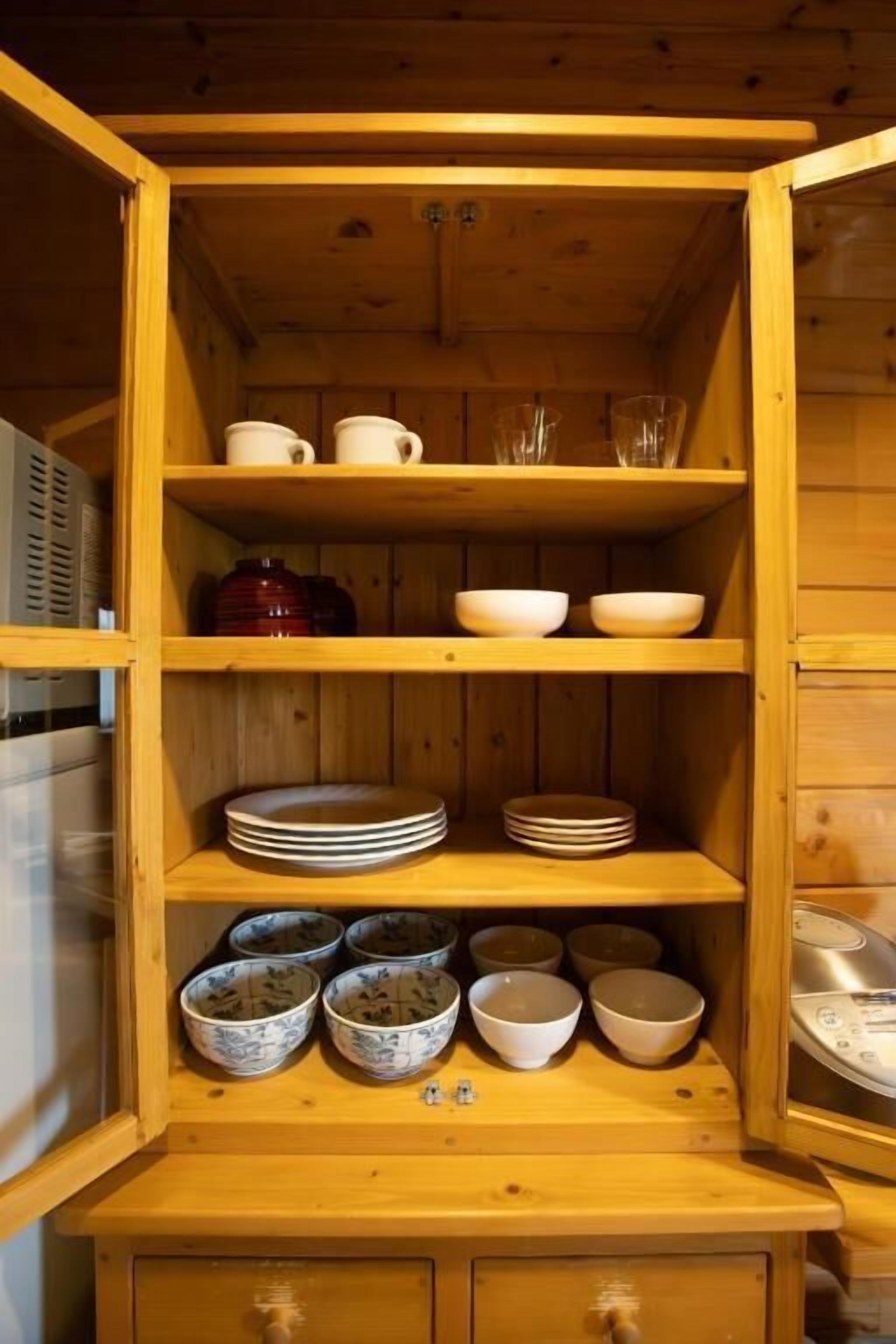 A wooden cabinet with shelves containing various kitchenware, including bowls, plates, and cups.