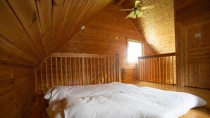 A wooden cabin room with a sloped ceiling, a bed with white bedding, and a window allowing natural light.