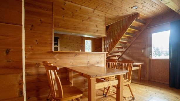A wooden cabin interior with a dining table and chairs, a staircase, and a window.