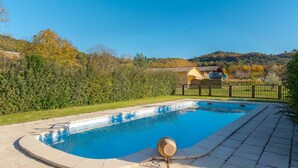 A swimming pool with a tiled deck, surrounded by a fence and trees. - Gîte 'Fleur De Thym' with Shared Pool, Communal Terrace and Air Conditioning (Gréoux-les-Bains)