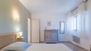 A bedroom with a bed, a nightstand, a dresser, a door, and a window. - Gîte 'Fleur De Thym' with Shared Pool, Communal Terrace and Air Conditioning (Gréoux-les-Bains)