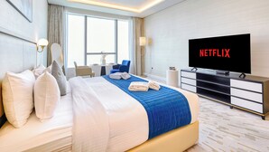 A modern hotel room with a large bed, a flat-screen TV, a desk, and a view of the city. - PVH - Inviting Studio - Palm Tower (Dubai)