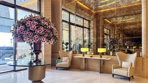 A modern lobby with a glass table, two armchairs, and a large floral arrangement. - PVH - Inviting Studio - Palm Tower (Dubai)