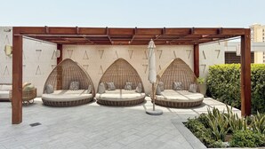 A covered outdoor seating area with three woven chairs and a central umbrella. - PVH - Inviting Studio - Palm Tower (Dubai)