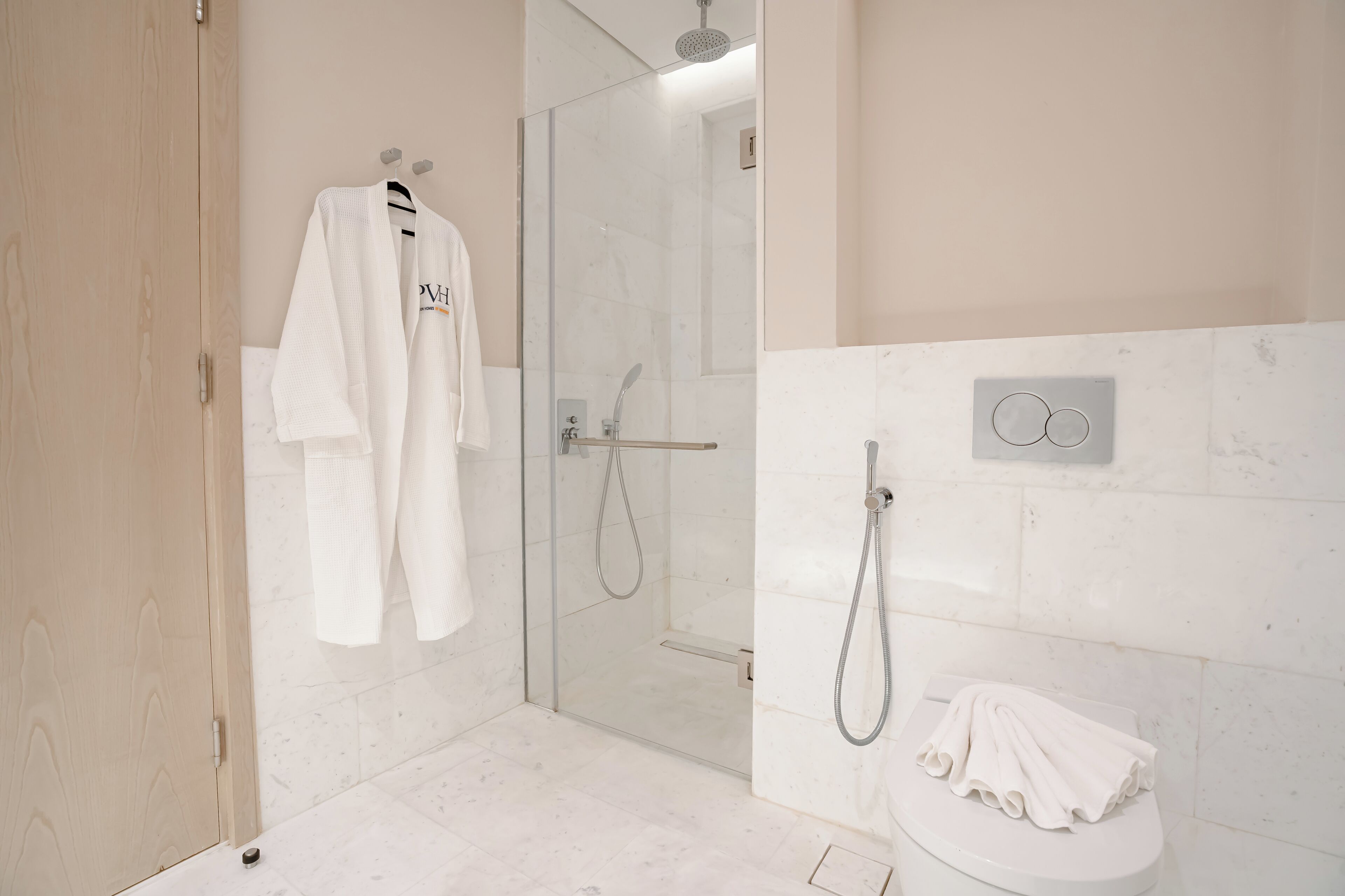A modern bathroom with a glass-enclosed shower, a toilet with a towel on it, and a robe hanging on a hook.