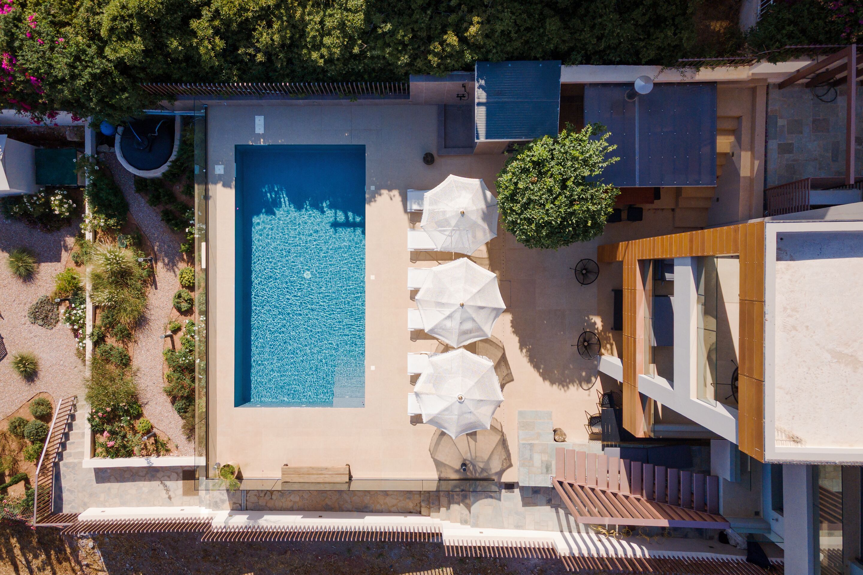 An aerial view of a modern hotel with a large swimming pool, outdoor seating, and lush landscaping.