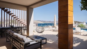 A covered outdoor seating area with a pool view, featuring a sofa, dining table, and chairs. - Villa Nefeli Athenian Riviera (Saronikos)