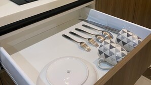 Een keuken met een wit aanrechtblad, een zwarte inductiekookplaat, een roestvrijstalen spoelbak en een lade met een wit bord, een witte kom, een lepel, een vork en een mes.