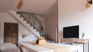 Een moderne woonkamer met een eettafel, stoelen, een televisie en een trap.