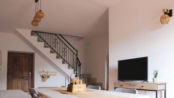 A modern living room with a dining table, chairs, a television, and a staircase.