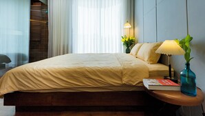 A neatly made bed with a beige comforter, a bedside lamp, a book, and a vase with a plant on a wooden nightstand. - Charming Private Room with Balcony – Local Homestay with Host Family, Cozy Stay (Tỉnh Thừa Thiên Huế)