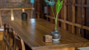 A wooden dining table with chairs, a vase with a plant, and a brick wall in the background. - Charming Private Room with Balcony – Local Homestay with Host Family, Cozy Stay (Tỉnh Thừa Thiên Huế)