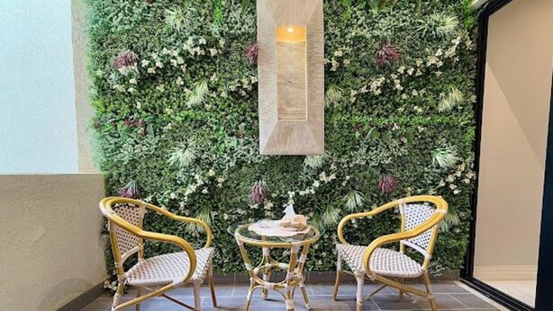 Un coin aménagé avec deux fauteuils en osier et une petite table ronde, un panneau en bois vertical et un mur végétal.