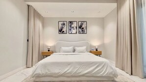 Une chambre à coucher moderne avec un grand lit, deux tables de chevet et trois œuvres d’art encadrées accrochées au mur.