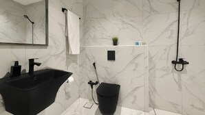 Une salle de bain avec un lavabo noir, un miroir, une serviette blanche, une petite plante et une douche.