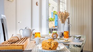 Una mesa de desayuno con pan, una tetera, una taza, un plato con un pastelito y un jarrón con flores secas.