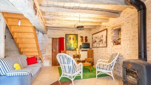 A cozy living room with a sofa, two white wicker chairs, a wooden staircase, a fireplace, and a painting on the wall. - Guest Room 'Chez Jacques - Zen' with Private Terrace, Wi-Fi and Air Conditioning (Saint-Martin-de-Fraigneau)
