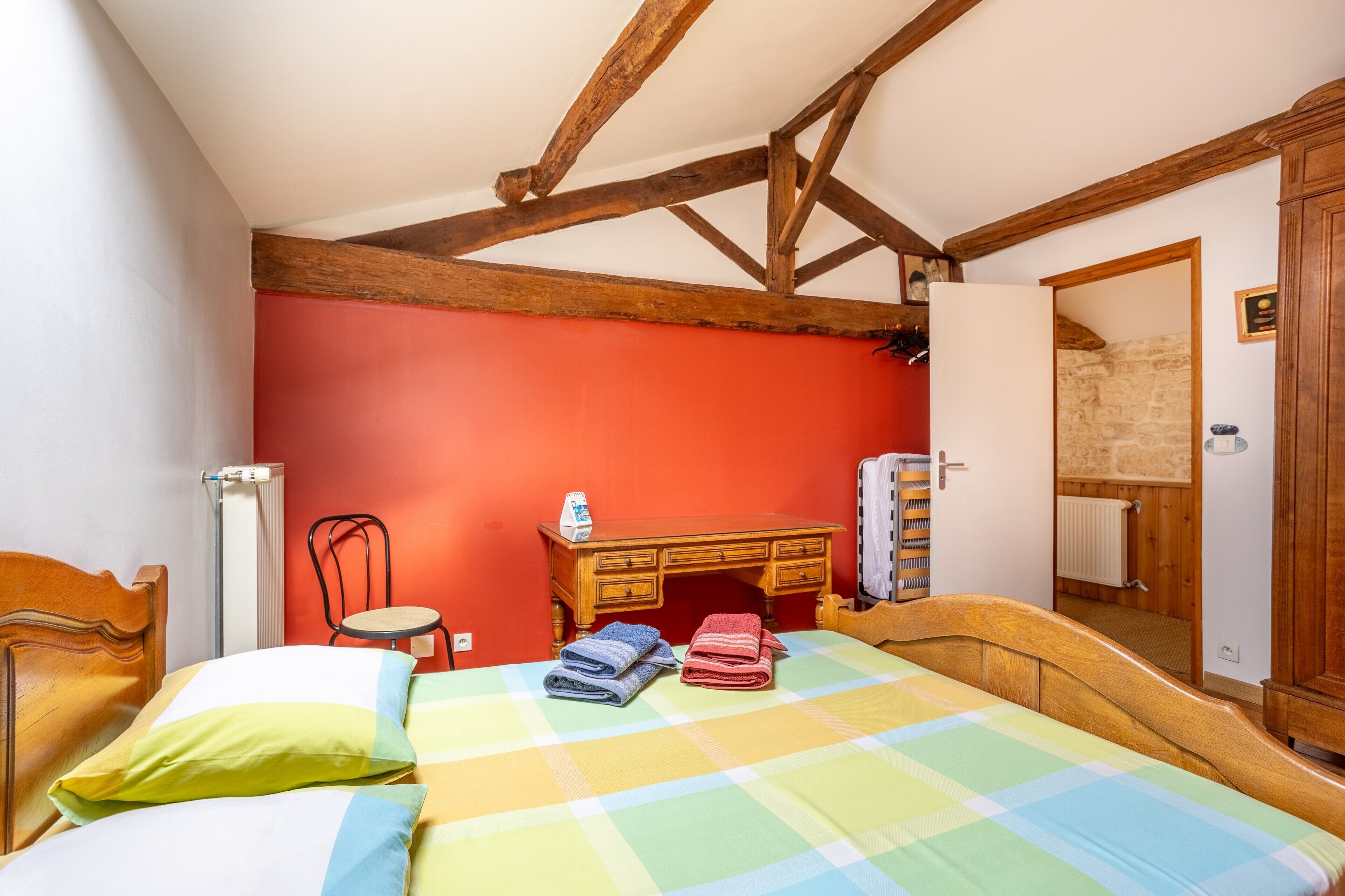 A bedroom with a wooden bed, a red wall, a wooden desk, and a mirror.