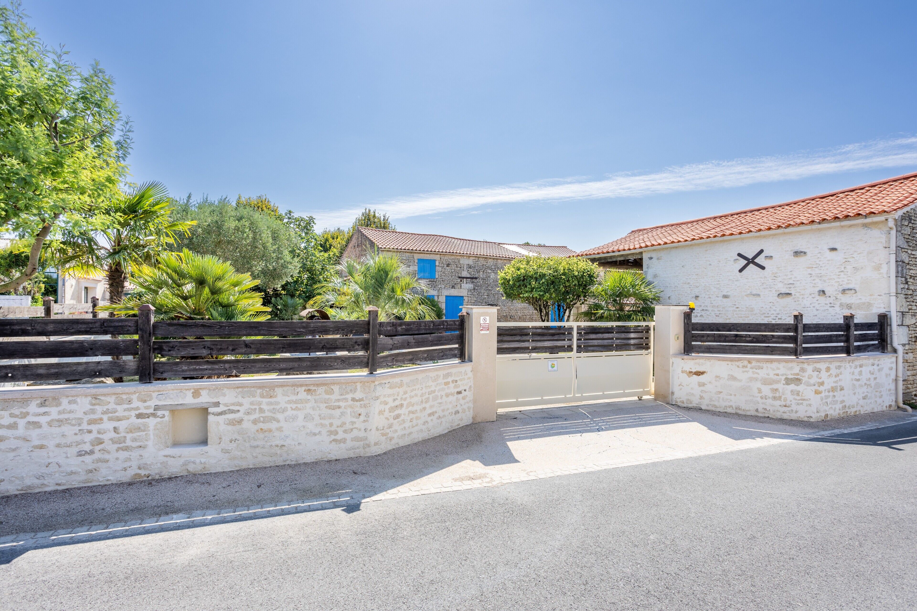 A gated entrance with a stone wall, a wooden fence, and a building with a tiled roof and a blue door.