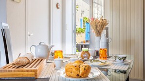 A breakfast table with bread, a teapot, a cup, a jar of jam, and a vase of dried flowers.