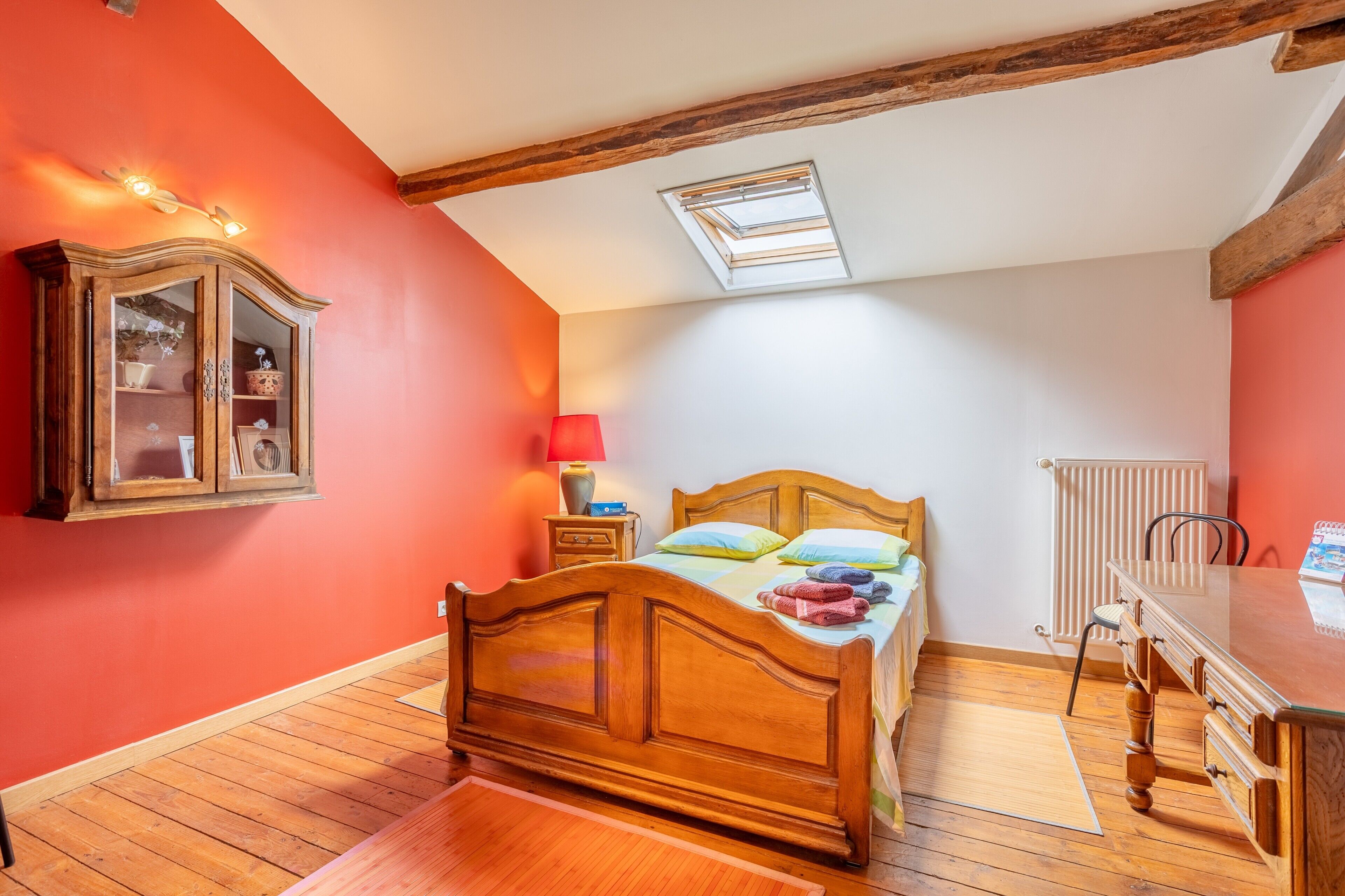 A bedroom with a wooden bed, a cabinet, a radiator, and a skylight.